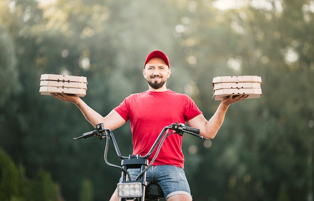 Gratis foto lage hoek smiley bezorger houden pizzadozen