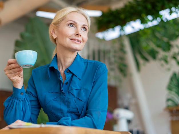 Gratis foto lage hoek van oudere zakenvrouw met kopje koffie tijdens het werken