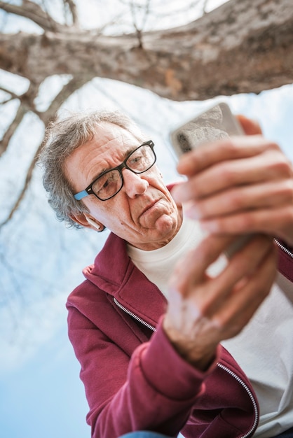 Lage hoekmening van de ernstige hogere mens die slimme telefoon met behulp van