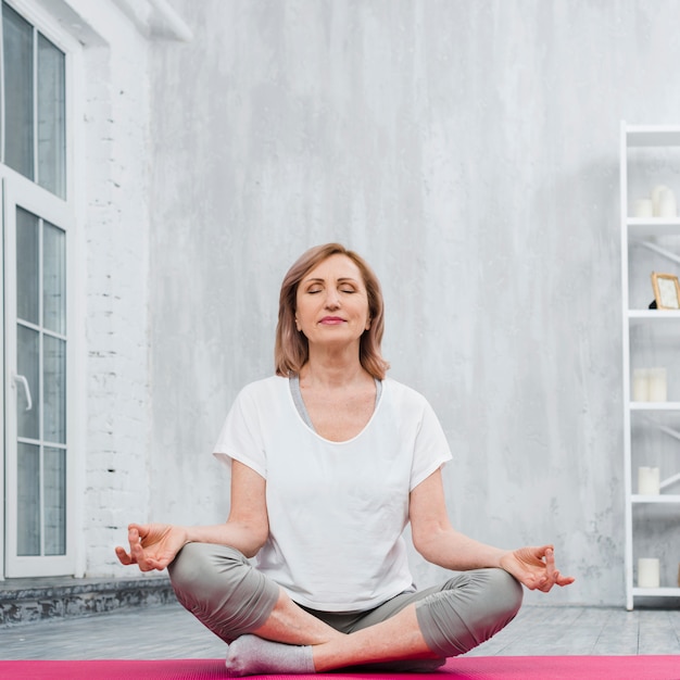 Lage hoekmening van een hogere vrouw die meditatie thuis doet