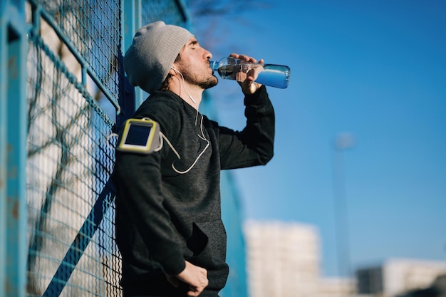 Lage hoekmening van jonge sportman die waterpauze heeft en zichzelf ververst met zoet water in de stad