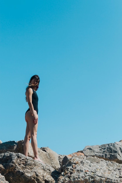 Lage hoekmening van vrouw in zwempak die zich op rots tegen blauwe hemel bevinden
