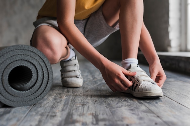 Lage sectie van een jongen die zijn schoenriem dichtbij de opgerolde oefeningsmat zet