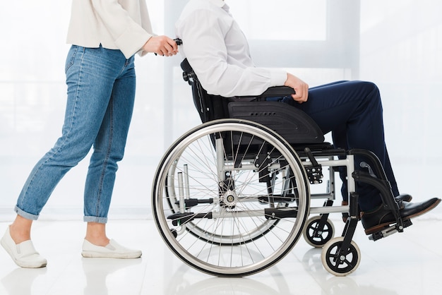 Lage sectie van een vrouw die de man zittend op rolstoel duwen