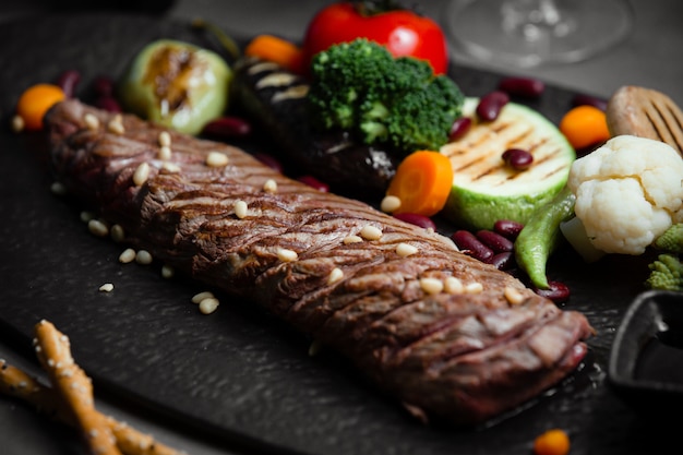 Gratis foto lam biefstuk met geroosterde en gegrilde groenten op zwarte stenen bord