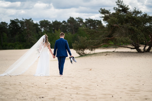 Landschap shot van een paar wandelen op zand op hun trouwdag