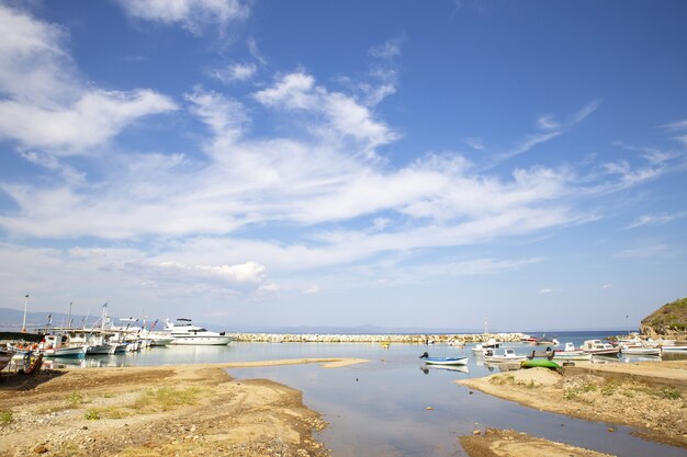 Landschap van de zee met boten erop omgeven door heuvels onder een blauwe hemel