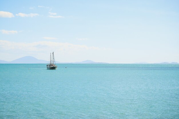 Landschap van de zee met een schip erop onder een blauwe lucht en zonlicht