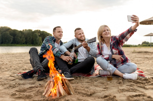 Lang geschoten vrienden die een selfie nemen terwijl ze op het zand zitten