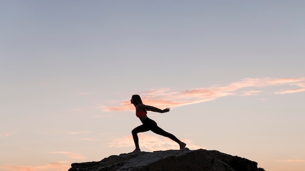 Gratis foto lang geschoten vrouw die zich in een sportpositie op een rots met exemplaarruimte bevindt