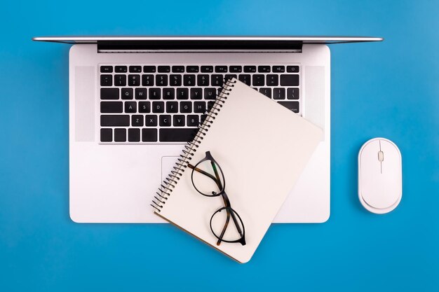 Laptop en blanco notitieblok op een blauwe achtergrond bovenaanzicht kopie ruimte