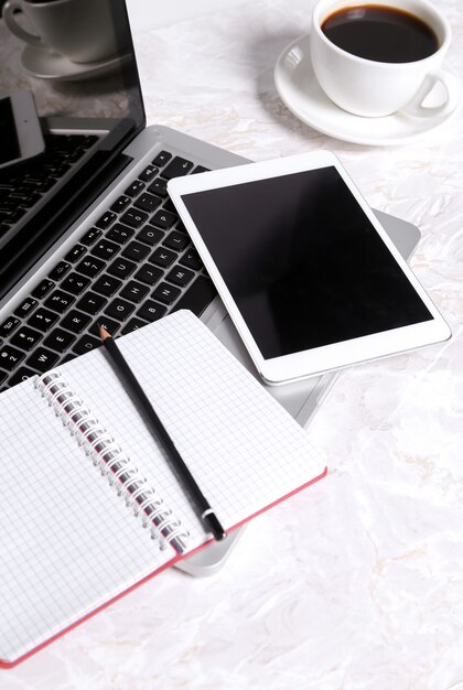 Laptop, Kladblok en pen op de tafel met een kopje koffie en met andere apparaten