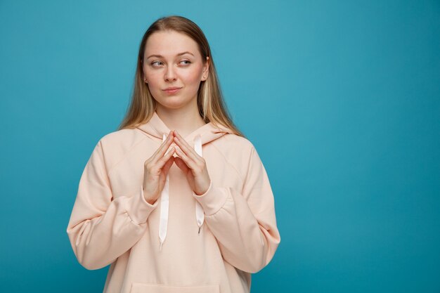 Lastige jonge blonde vrouw die handen samen houdt die kant bekijken