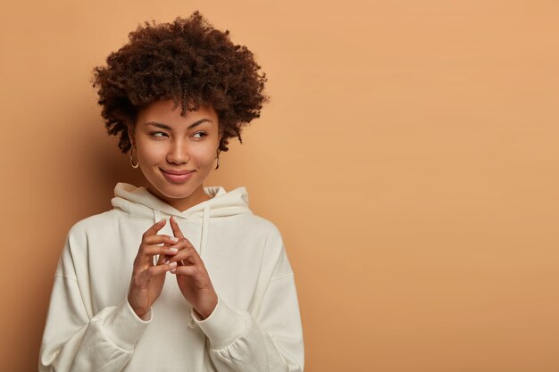 Lastige zwarte vrouw heeft een groot kwaadaardig plan, houdt de handen bij elkaar en kijkt met de bedoeling iets te doen, is van plan iets interessants te doen