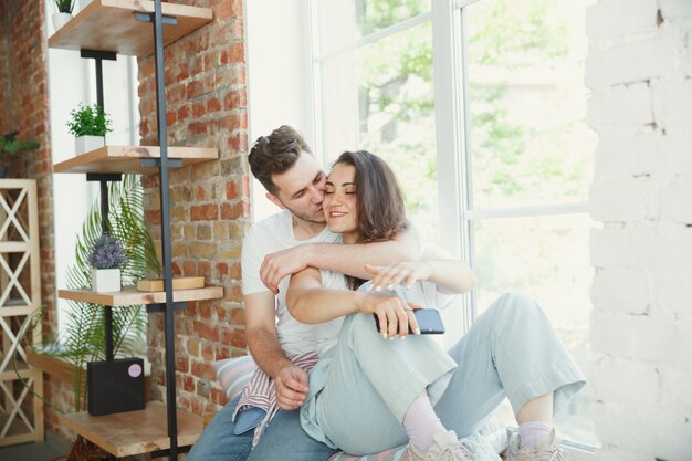 Laten we dit moment bekijken. Jong stel verhuisde naar een nieuw huis of appartement. Zie er gelukkig en zelfverzekerd uit. Familie, verhuizen, relaties, eerste huisconcept. Bij het raam zitten, knuffelen en selfie maken.