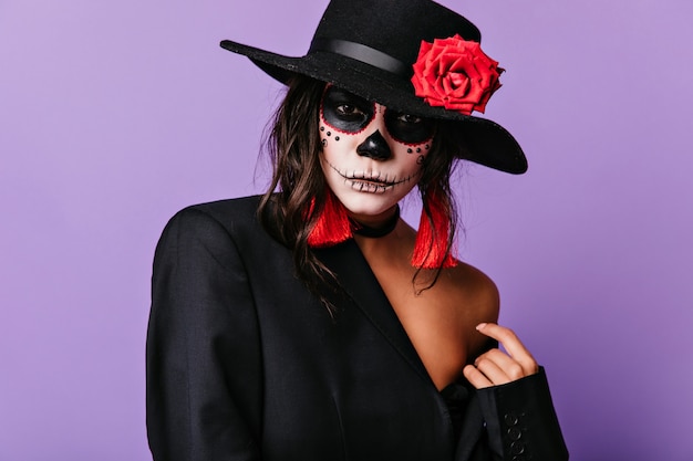 Latijnse vrouw in zwarte jas en sombrero. Tevreden meisje in muertosuitrusting die op halloween wacht.