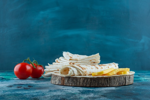 Lavash en kaas op een bord naast tomaten, op de blauwe achtergrond.