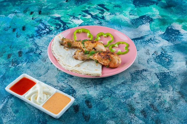 Lavash, gekookte drumsticks en peper op een bord naast sauskommen op het blauwe oppervlak
