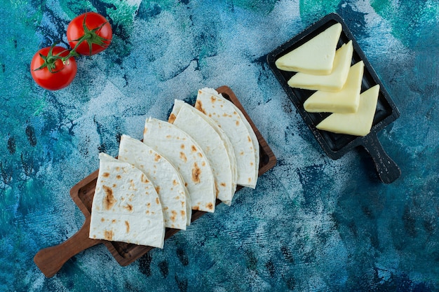 Gratis foto lavash op een bord en heerlijke kaas op een bord naast tomaten, op de blauwe achtergrond.