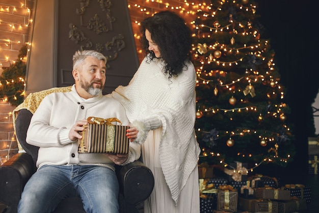 Leeftijd en mensen concept. Hoger paar met giftdoos over lichtenachtergrond. Vrouw in een witte gebreide trui.