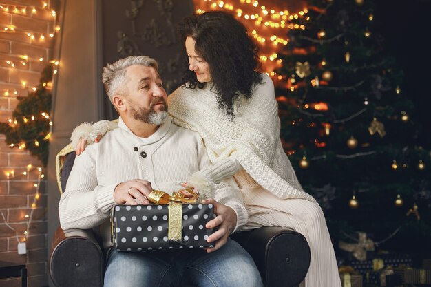 Leeftijd en mensen concept. Hoger paar met giftdoos over lichtenachtergrond. Vrouw in een witte gebreide trui.