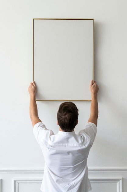 Gratis foto leeg frame wordt opgehangen door een jonge man aan een witte minimale muur