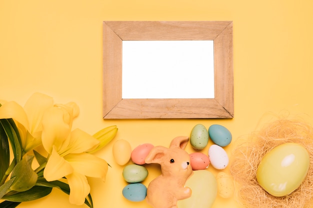 Leeg houten wit frame met paaseieren; konijntjesnest en leliebloem op gele achtergrond