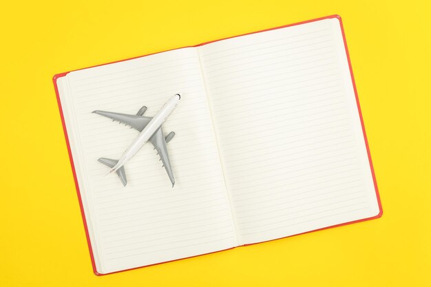 Leeg notitieboekje en vliegtuigmodel op gele vlakke achtergrond