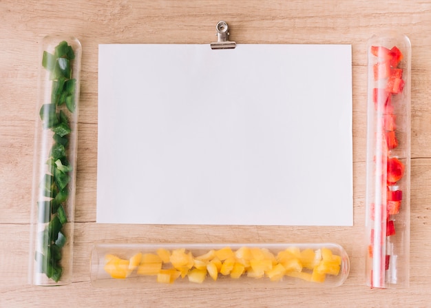 Gratis foto leeg wit papier omgeven door transparante reageerbuisjes met plakjes groen; gele en rode paprika's