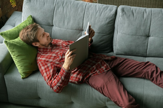 Leesboek op de bank. Blanke man blijft thuis tijdens quarantaine