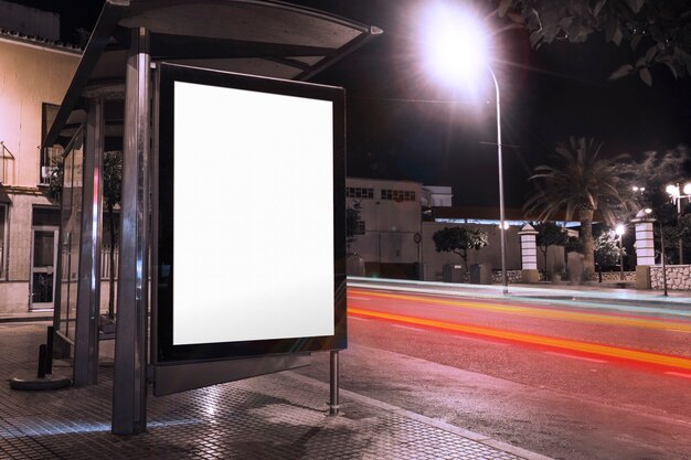 Lege advertentie bij bushokje met vage verkeerslichten bij nacht