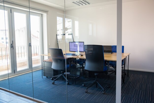 Lege directiekamer achter glazen wand. Vergaderruimte met vergadertafel, gedeeld bureau voor team en werkplekken. Handel in grafieken op monitor. Kantoorinterieur of commercieel vastgoedconcept