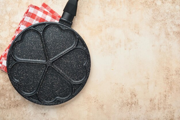 Lege koekenpan zwart, koekenpan met stenen anti-aanbaklaag voor het bakken van pannenkoeken in de vorm van ontbijtharten en ingrediënten op grijze betonnen tafelondergrond. ontbijt voor valentijnsdag. bovenaanzicht.