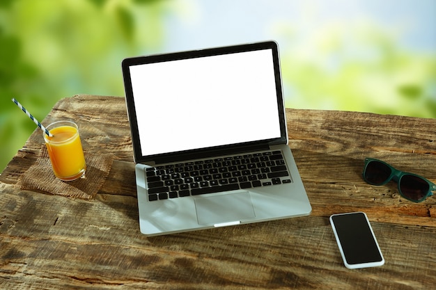 Lege schermen van laptop en smartphone op een houten tafel buiten met de natuur op de muur, mock up.