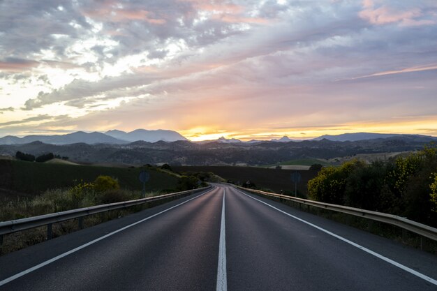 Lege snelweg omgeven door heuvels onder de bewolkte avondrood