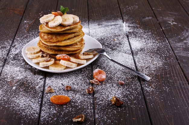 Lekker ontbijt. Heerlijke puncakes met bananen, noten en munt die op witte plaat worden gediend