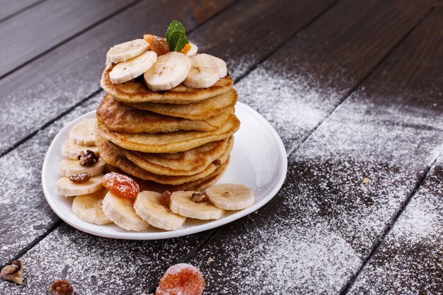 Lekker ontbijt. Heerlijke puncakes met bananen, noten en munt die op witte plaat worden gediend