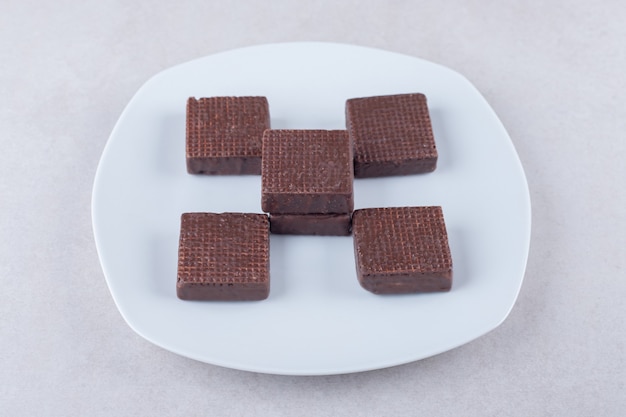 Lekkere chocolade gecoate wafeltjes op een bord op marmeren tafel.