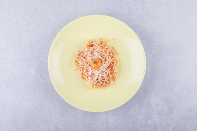 Lekkere gekookte spaghetti met tomaten op gele plaat.