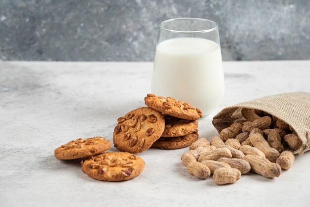 Lekkere koekjes met honing en pinda's en glas melk op marmeren tafel.