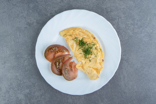 Lekkere omelet en tomaat plakjes op witte plaat.