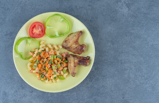 Lekkere pasta en kippenvleugels op gele plaat.