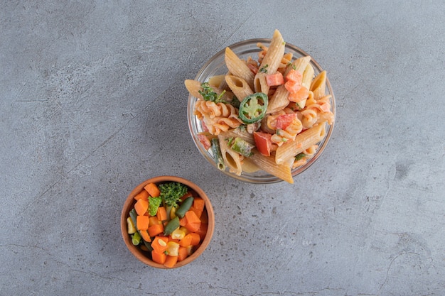 Lekkere penne pasta en frisse salade op stenen achtergrond.