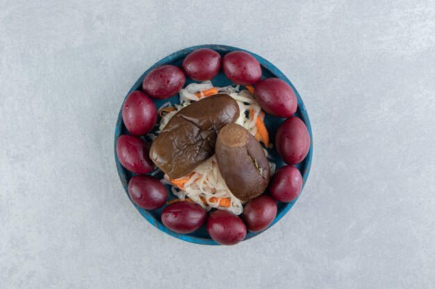 Lekkere zuurkool, aubergine en pruimen op blauw bord.