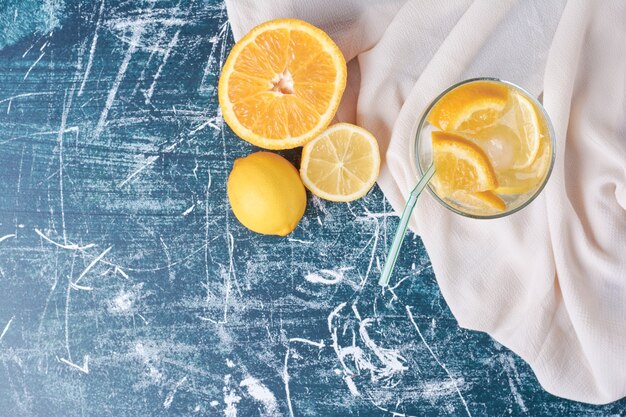 Lemonnd sinaasappels met een kopje drank op blauw.