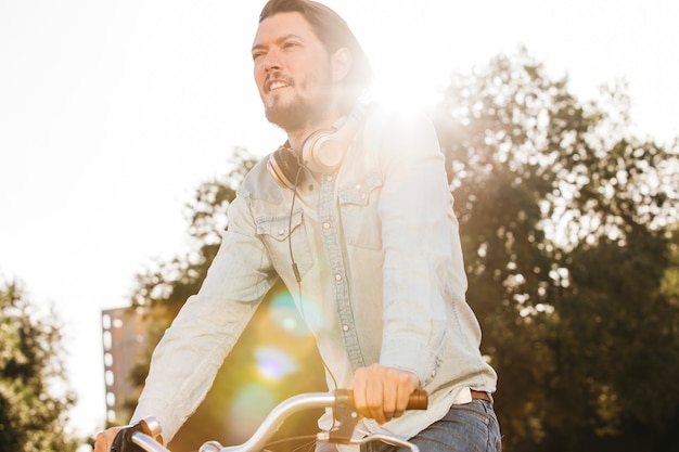 Lensflare die over de modieuze jonge man met hoofdtelefoon rond zijn hals berijdende fiets valt