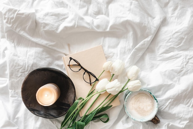 Gratis foto lente achtergrond met een boeket tulpen een kopje koffie en een boek in een bed