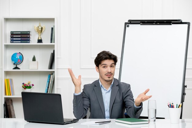 Leraar jonge instructeur in kantoorpak in de klas met laptop en whiteboard zwaaiende handen