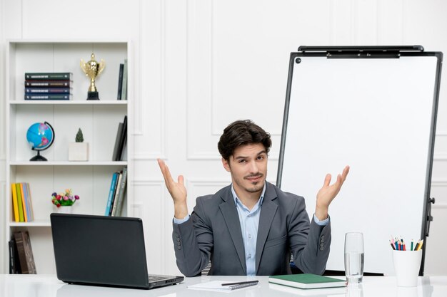 Leraar jonge instructeur in kantoorpak in de klas met laptop en whiteboard zwaaiende handen