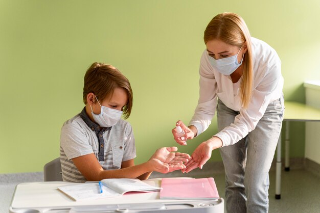 Leraar met medische masker handen van het kind desinfecteren in de klas